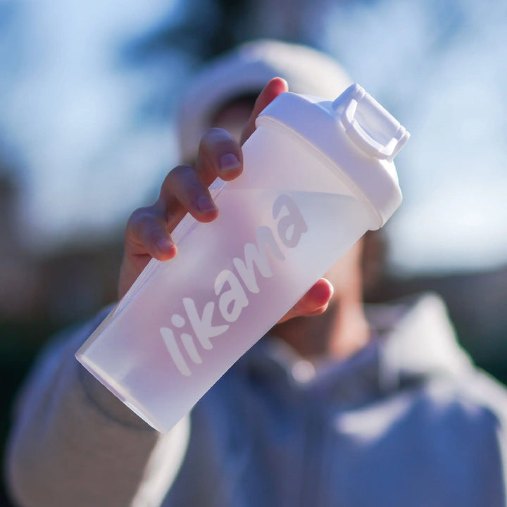 Shaker Likama transparent tenu en main en extérieur, illustrant la praticité et l’hydratation pendant ou après l’entraînement sportif