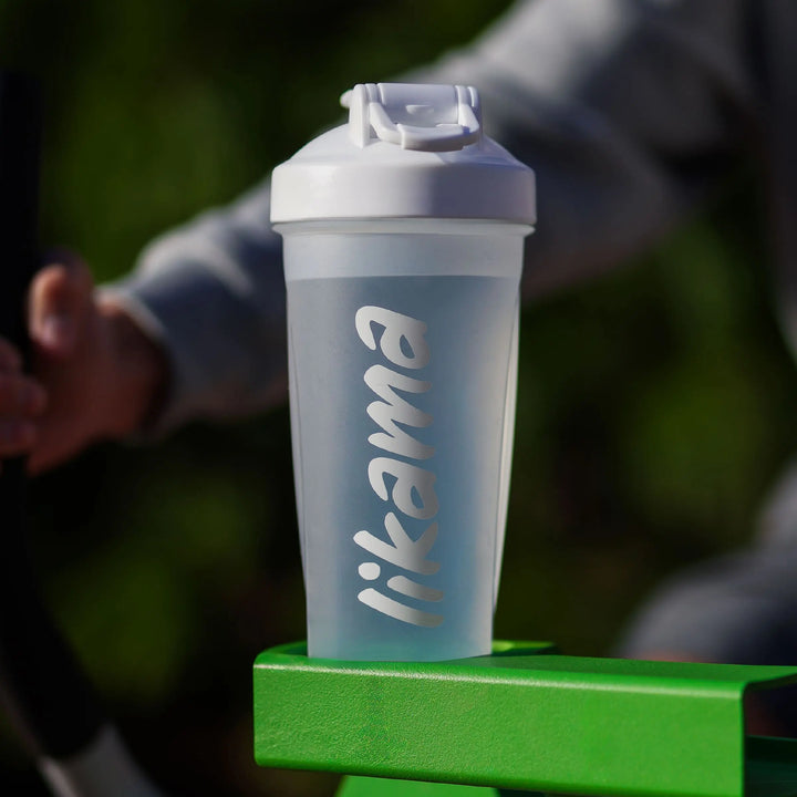 Shaker transparent de la marque Likama posé sur un appareil de sport vert, illustrant la praticité et l’hydratation pendant une activité physique